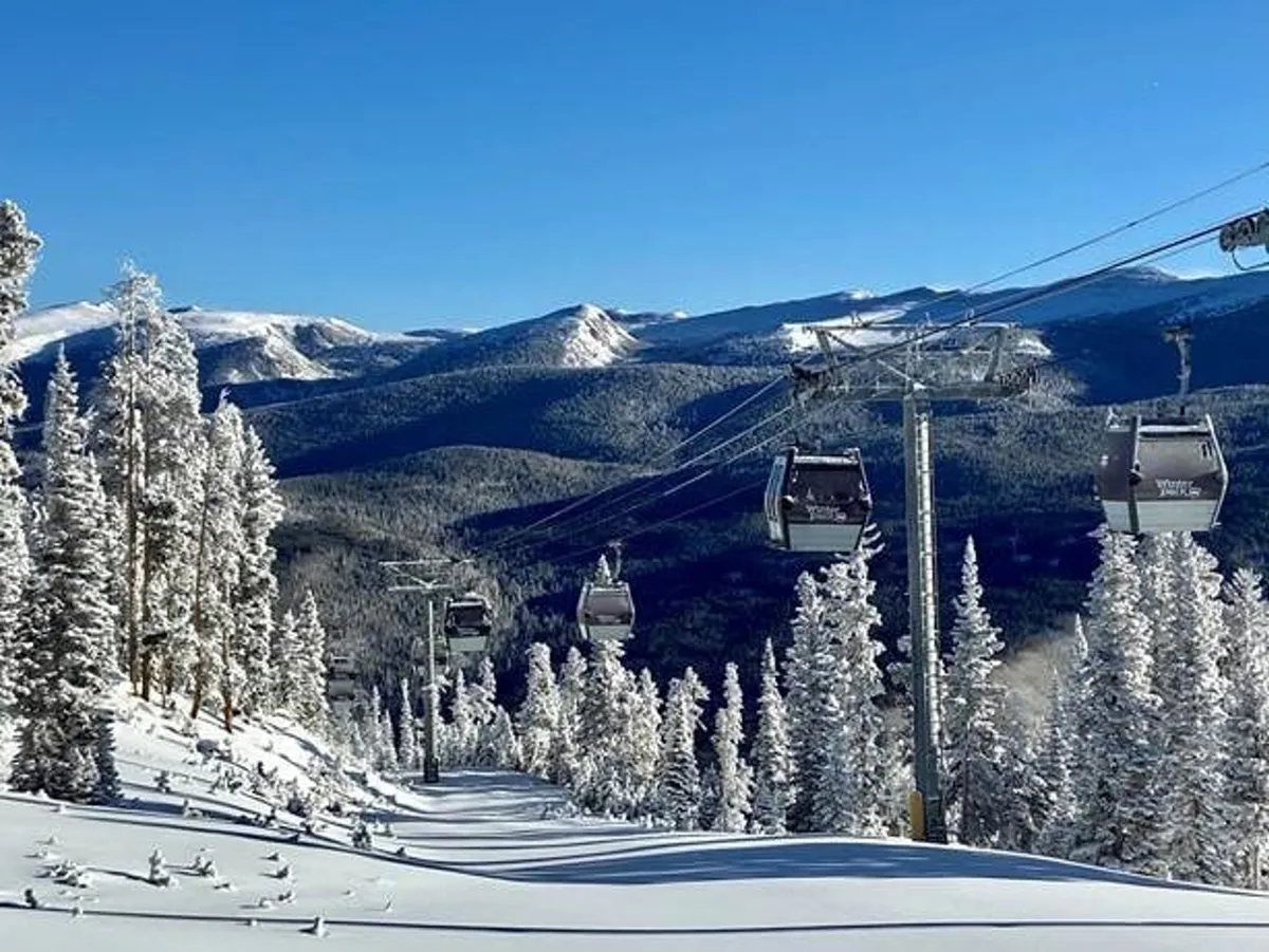 An exterior view featuring ski gondolas gliding over a snow-covered landscape, with majestic mountain ranges and snow-dusted trees under a clear blue sky. The setting exudes both serenity and the thrill of winter sports, evoking the proximity of Winter Park Resort and access to snow-bound adventures.