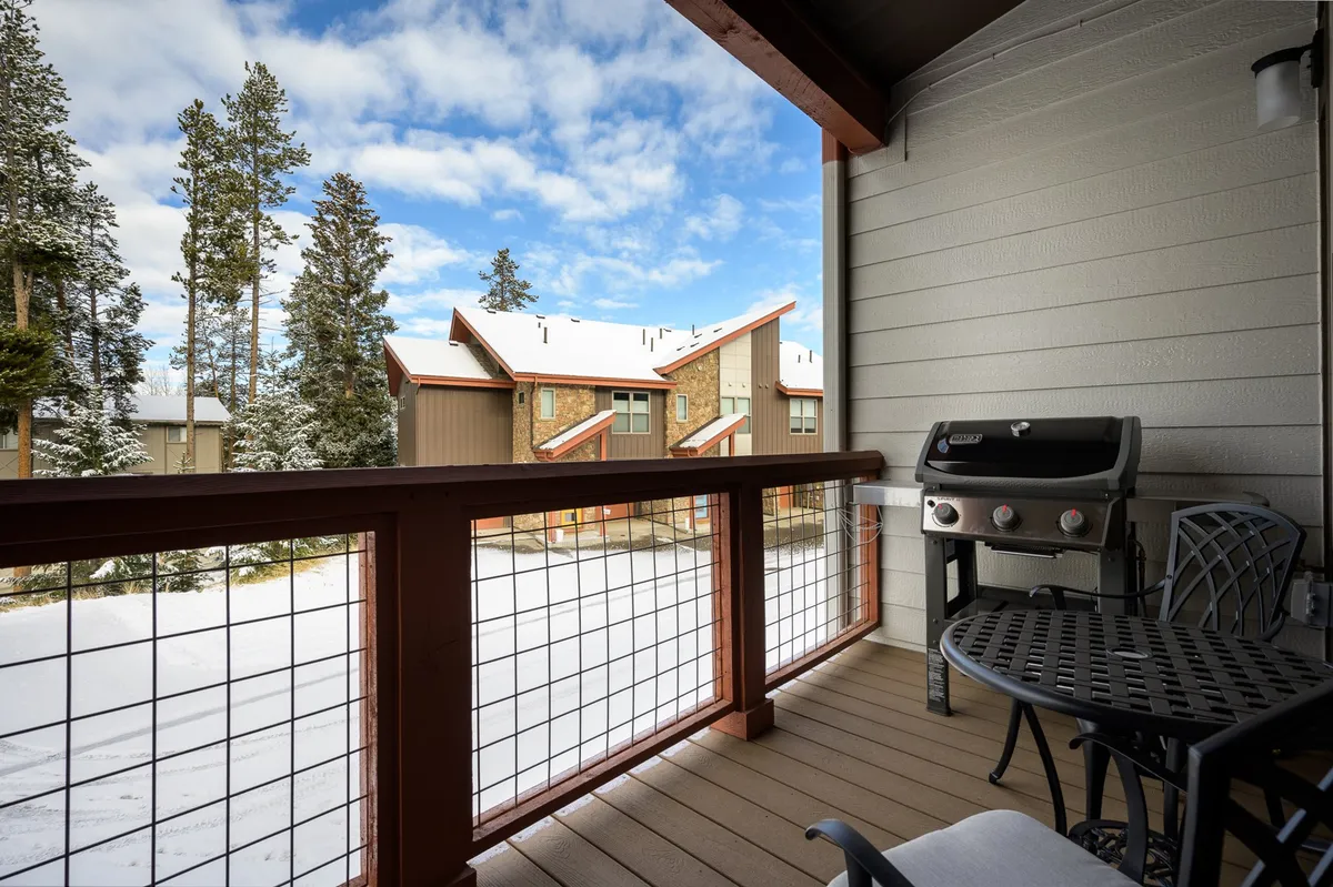 A cozy patio area with a grill, table, and chairs, framed by snow-covered trees and neighboring homes. The setting invites both quiet moments and social gatherings, all while surrounded by natural beauty.