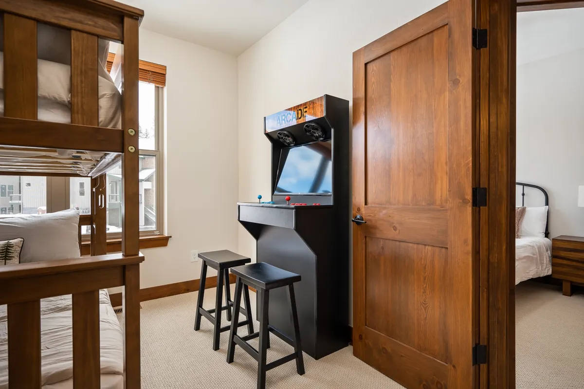A playful interior featuring a bunk bed and an arcade game machine set against a wooden door. The setup invites both rest and entertainment, creating a fun, family-friendly atmosphere ideal for game nights and late-night competitions.