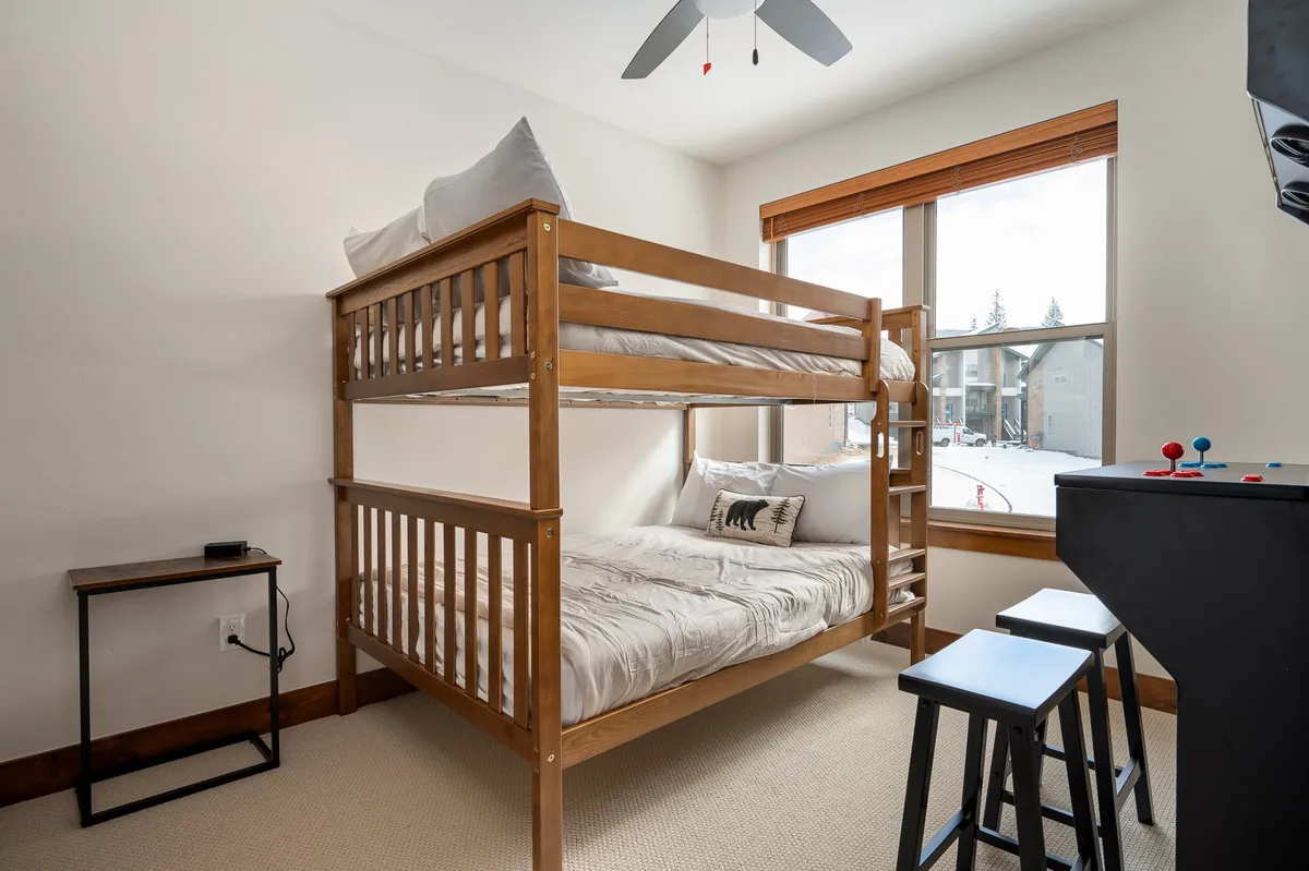 A playful and inviting bunk room, complete with a bunk bed, window view of snowy landscapes, a small table, and stools. The room has a cheerful vibe, making it perfect for kids or friends to bond and create memories.