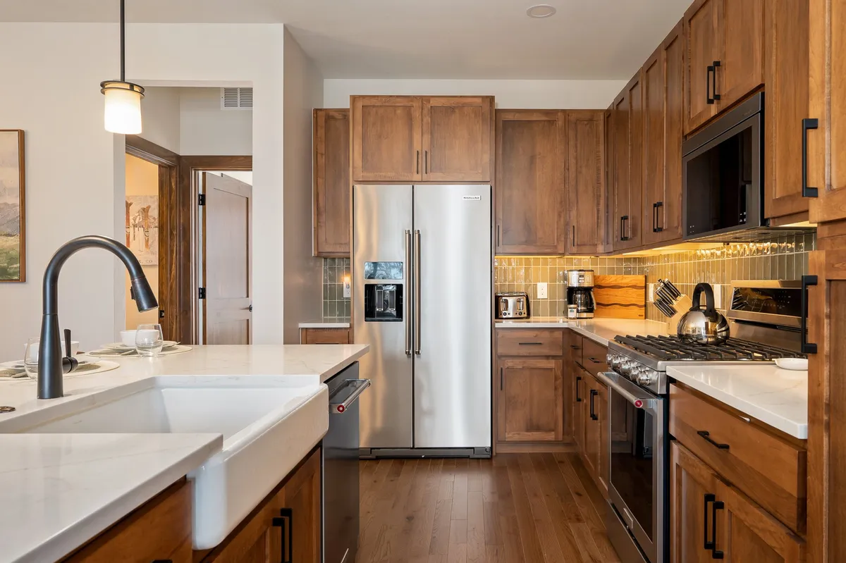 A stylish kitchen with sleek stainless steel appliances, wood cabinetry, and crisp white countertops. The layout provides generous space for cooking, gathering, and enjoying meals with friends or family.