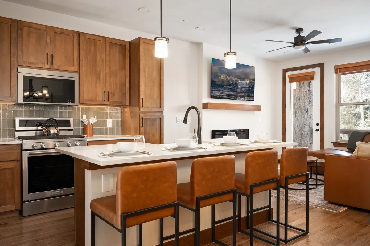 A warm, inviting kitchen with a spacious kitchen island, bar stools, stainless steel appliances, wood cabinetry, and art adorning the walls. The space is designed for cooking, entertaining, and socializing, with ample counter space and seating for casual dining or group gatherings.