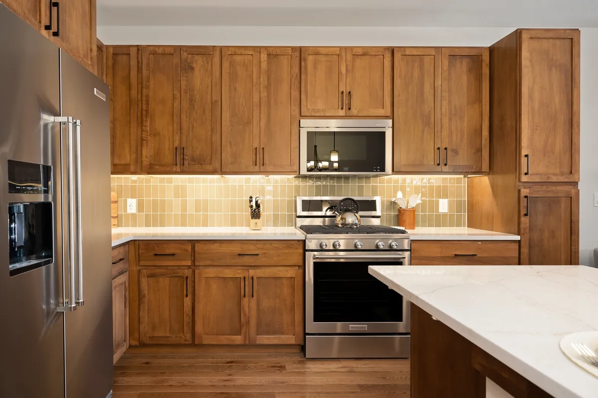 A cozy, well-appointed kitchen with stainless steel appliances, marble countertops, attractive wall tiles, and warm wood cabinetry. The ambiance encourages both everyday cooking and special-occasion meal preparation with family or friends.
