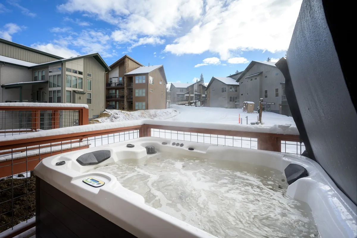 A tranquil outdoor scene with a brand-new hot tub nestled into a snow-covered landscape, surrounded by nearby buildings. The bubbling water offers a warm retreat, ideal for relaxing after a day of adventure.
